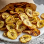Crispy golden Air Fryer Banana Chips spilling out of a brown paper bag onto a white plate, ready for a healthy snack.