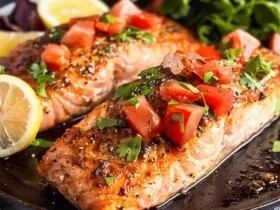 Cooked air fryer frozen salmon garnished with tomatoes and herbs, accompanied by lemon slices.