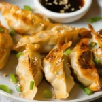 A plate of Air Fryer Ling Ling Potstickers with sesame seeds and green onions, served with dipping sauce.
