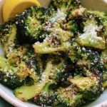 A bowl of perfectly roasted Air Fryer Parmesan Broccoli garnished with a fresh lemon wedge and grated cheese.