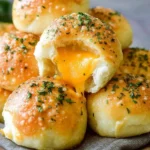 A pile of golden-brown GARLIC BUTTER CHEESE BOMBS, one torn open to reveal gooey melted cheddar cheese oozing out, garnished with green herbs.