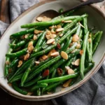 A ceramic bowl filled with vibrant green beans topped generously with toasted slivered almonds, ready to serve.