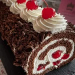 A delicious Black Forest Cake Roll covered in chocolate shavings, topped with whipped cream swirls and cherries, showing its cherry and cream filling.