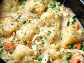 crockpot chicken and dumplings 53 A close-up of a creamy crockpot chicken and dumplings dish, featuring tender chicken, fluffy dumplings, carrots, peas, and fresh chives.