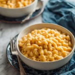 Two bowls of golden, creamy Crockpot Mac and Cheese with elbow macaroni, served on patterned blue plates with a fork.