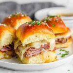Savory french dip sliders with thinly sliced roast beef, melted cheese, and onions on golden buns, sprinkled with parsley and sea salt.