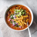 A vibrant bowl of homemade taco soup topped with diced avocado, red onion, fresh cilantro, and crispy tortilla strips.