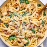 A creamy tuscan chicken pasta dish with penne, spinach, sun-dried tomatoes, and grilled chicken, topped with grated cheese.