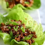 Close-up of two vibrant Asian Chicken Lettuce Wraps, filled with seasoned ground meat and topped with sesame seeds and green onions.
