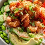 A vibrant Bang Bang Shrimp Bowl featuring crispy shrimp, avocado, cucumber, edamame, and carrots over rice, drizzled with sauce.