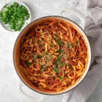 A white pot filled with homemade Bolognese Pasta, garnished with fresh parsley and cheese, viewed from above.