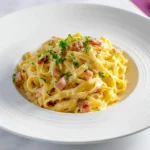 A delectable plate of creamy fettuccine Carbonara, garnished with crispy bacon bits and fresh parsley, served in a white bowl.