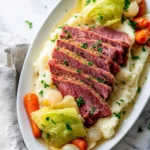 A delicious plate of sliced Crockpot Corned Beef And Cabbage served with creamy mashed potatoes, carrots, and pearl onions.