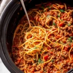 A close-up view of a large black slow cooker filled with hearty Crockpot Spaghetti and a serving fork lifting some noodles.