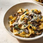 A rustic bowl of creamy Garlic Mushroom Pasta, featuring wide noodles, sautéed mushrooms, fresh parsley, and grated Parmesan cheese.
