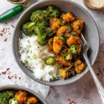 A grey bowl filled with white rice, steamed broccoli, and spicy jalapeno chicken, garnished with fresh jalapeno slices.