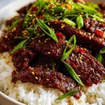 Delicious Korean Beef Bulgogi served over white rice, garnished with green onions, red chili, and sesame seeds in a white bowl.