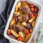 A white rectangular baking dish filled with beautifully roasted mediterranean chicken thighs, potatoes, red onions, tomatoes, and carrots, garnished with fresh thyme sprigs.