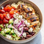 A colorful and vibrant mediterranean chicken bowl with grilled chicken, quinoa, tomatoes, cucumbers, red onion, feta, and olives.