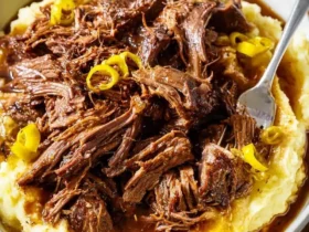 A hearty bowl of tender Mississippi Pot Roast shredded over creamy mashed potatoes, topped with gravy and pickled peppers, with a fork.