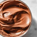 A close-up overhead view of rich, creamy Ninja Creami Chocolate Ice Cream swirled beautifully in a clear glass jar.