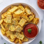 A white bowl filled with golden, crispy pasta chips, generously sprinkled with grated parmesan and fresh parsley, served with two small bowls of marinara sauce.
