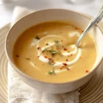 Close-up of a delicious bowl of pear potato soup, elegantly garnished with a cream swirl, thyme, and red chili flakes.