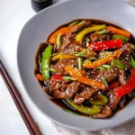 A beautifully presented Pepper Steak dish with tender beef, colorful bell peppers, and a glossy sauce, garnished with sesame seeds and green onions.