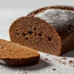 A freshly sliced loaf of dark pumpernickel bread, revealing its dense crumb and a light dusting of flour.