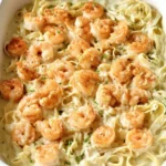 A close-up shot of a white baking dish brimming with a creamy Seafood Alfredo Casserole, featuring fettuccine pasta and seasoned shrimp.