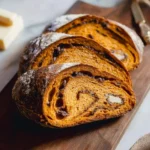 Slices of Artisan Pumpkin Sourdough Bread with chocolate chips and butter, dusted with powdered sugar on a wooden board.