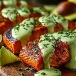 Pan-seared Cajun Salmon fillets topped with creamy avocado lime sauce, garnished with fresh lime wedges and cilantro on a wooden board.