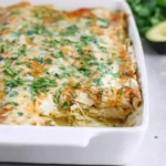 A close-up of a bubbling hot green chicken enchilada casserole in a white baking dish, topped with melted cheese and fresh cilantro.