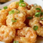 A close-up shot of a white plate piled high with golden-fried Honey Walnut Shrimp, garnished with chopped green onions and walnuts.