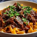 A close-up of a white bowl overflowing with savory Korean Beef Noodles, featuring tender beef, wide pasta, fresh herbs, and sesame seeds.