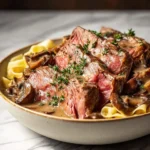 Delicious slices of Leftover Prime Rib with creamy mushroom sauce and wide pasta, garnished with fresh herbs in a bowl.
