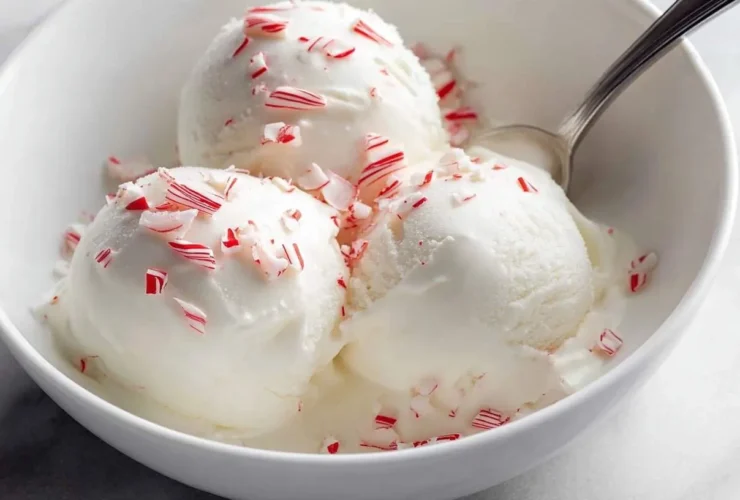 Three scoops of creamy white Ninja Creami Peppermint Ice Cream topped with crushed peppermint candy pieces in a white bowl with a spoon.