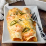 Two cheesy Shrimp Enchiladas topped with creamy sauce, succulent shrimp, and fresh jalapeño slices on a white plate.