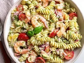 A vibrant bowl of Shrimp Pasta Salad with fusilli, cherry tomatoes, red onion, and a fresh basil garnish.
