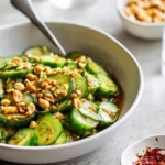 A white bowl filled with a vibrant Spicy Peanut Cucumber Salad, featuring sliced cucumbers, crushed peanuts, and red chili flakes in a rich sauce.