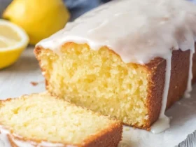 A delicious Starbucks Copycat Lemon Loaf with a thick glaze, partially sliced, showing its moist yellow interior, with fresh lemons in the background.