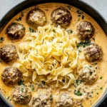 Overhead view of a white Dutch oven filled with rich swedish meatball soup with creamy sauce, tender meatballs, and egg noodles, garnished with fresh parsley.