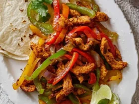 Close-up of a white platter featuring vibrant Air Fryer Chicken Fajitas with seasoned chicken, colorful peppers, onions, lime, and tortillas.