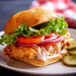 A crispy Air Fryer Chicken Sandwich with lettuce, tomato, onion, and creamy sauce on a golden bun, served with pickles.