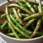 White bowl filled with perfectly roasted Air Fryer Green Beans, vibrant green with savory, slightly charred edges.