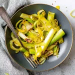 A close-up shot of a dark grey bowl filled with tender, seasoned Air Fryer Leeks, showing some browned edges, with a fork resting inside.
