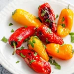 A white plate displays vibrant red and yellow Air Fryer Mini Peppers, perfectly roasted and garnished with fresh green herbs.