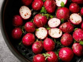 A close-up view of vibrant red whole and halved radishes seasoned with herbs in an air fryer basket, ready to be cooked as Air Fryer Radishes.