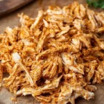 A large pile of seasoned Air Fryer Shredded Chicken rests on a rustic wooden cutting board, ready for use.