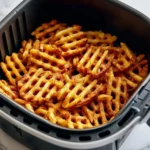 A close-up view of golden, crispy Air Fryer Waffle Fries perfectly cooked inside a black air fryer basket, ready to eat.